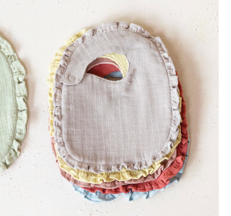 Creative Co-Op Cotton Double Cloth Baby Bibs stacked, with ruffled edges in tan, sage, yellow and rust and a toucan patch