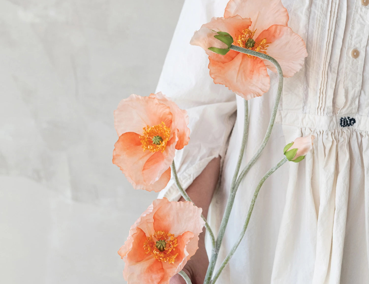 Person in a white dress holding Creative Co-Op Faux Poppy Flowers in coral