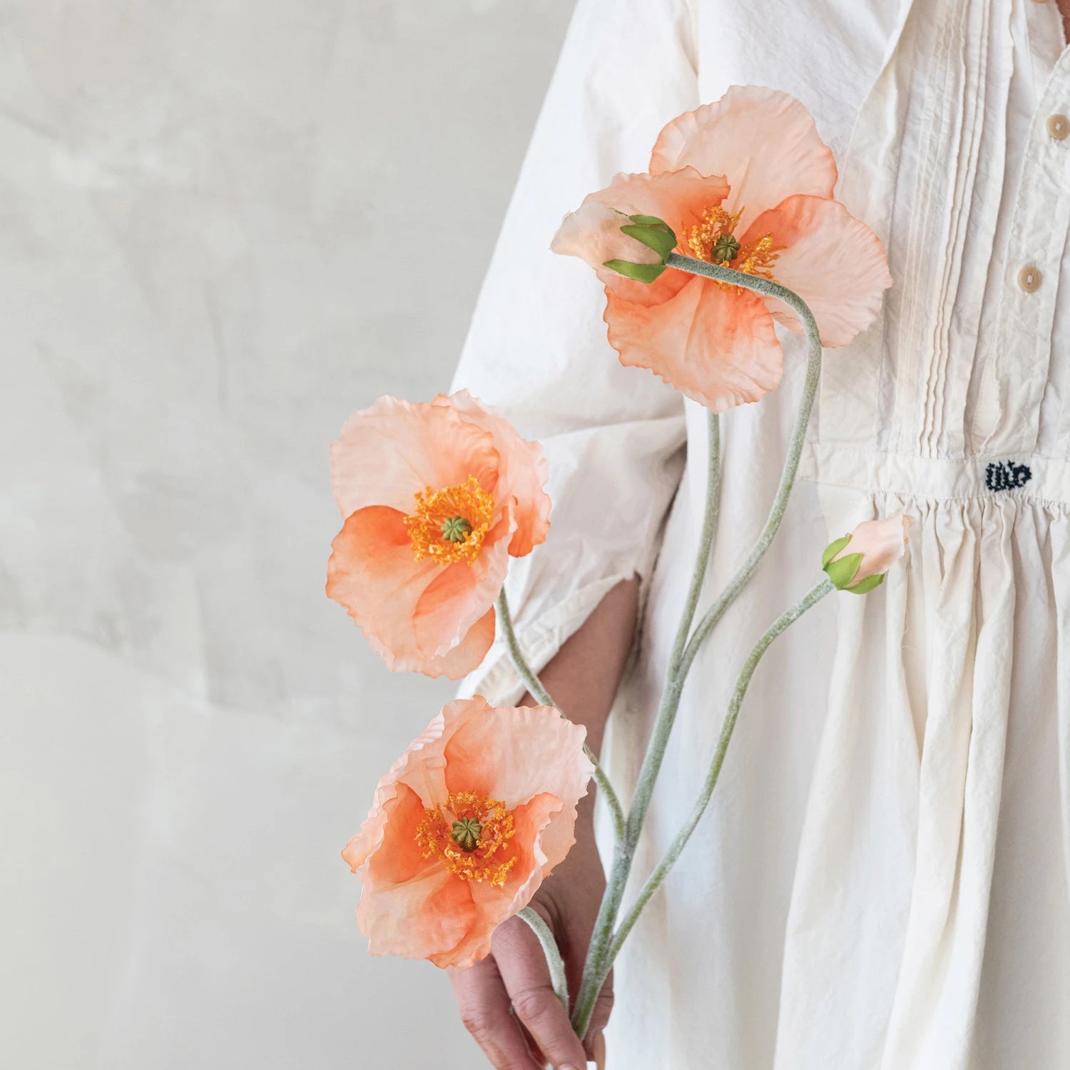 Person in a white dress holding Creative Co-Op Faux Poppy Flowers in coral