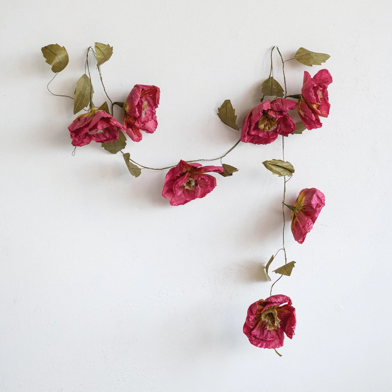 Creative Co-Op Paper Flower Garland hung on a white wall, full view