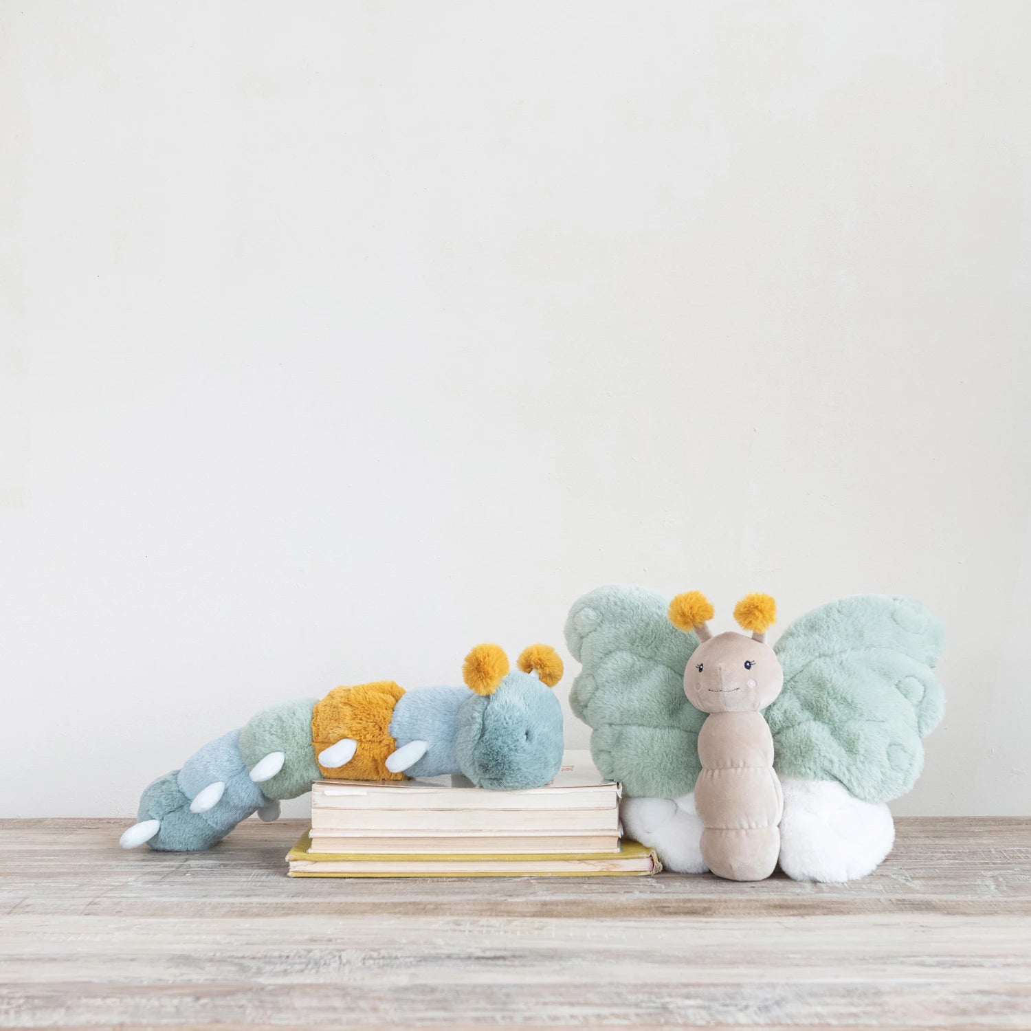 Creative Co-Op Plush Caterpillar and a plush butterfly on a wood floor with books