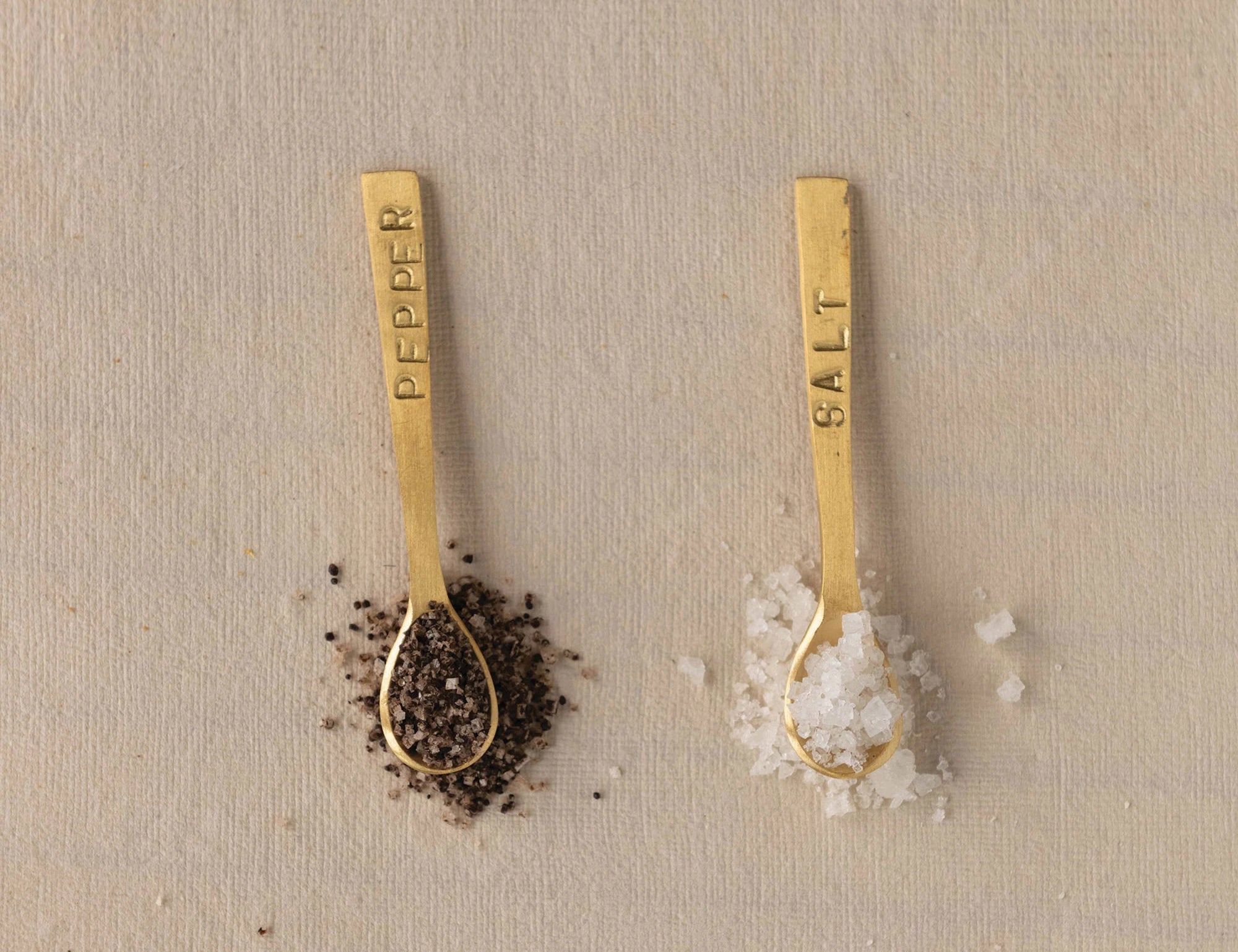 Creative Co-Op Salt and Pepper brass spoons holding peppercorns and coarse salt