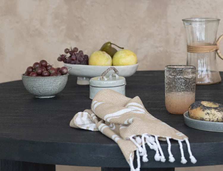 Creative Co-Op Stoneware Jar with Rattan Handle on a black table with fruit and a linen towel