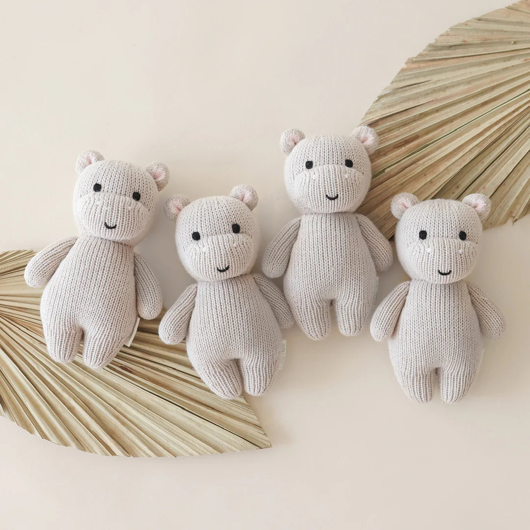 Cuddle & Kind Baby Hippo knit dolls, four cream hippos arranged with dried palm leaves