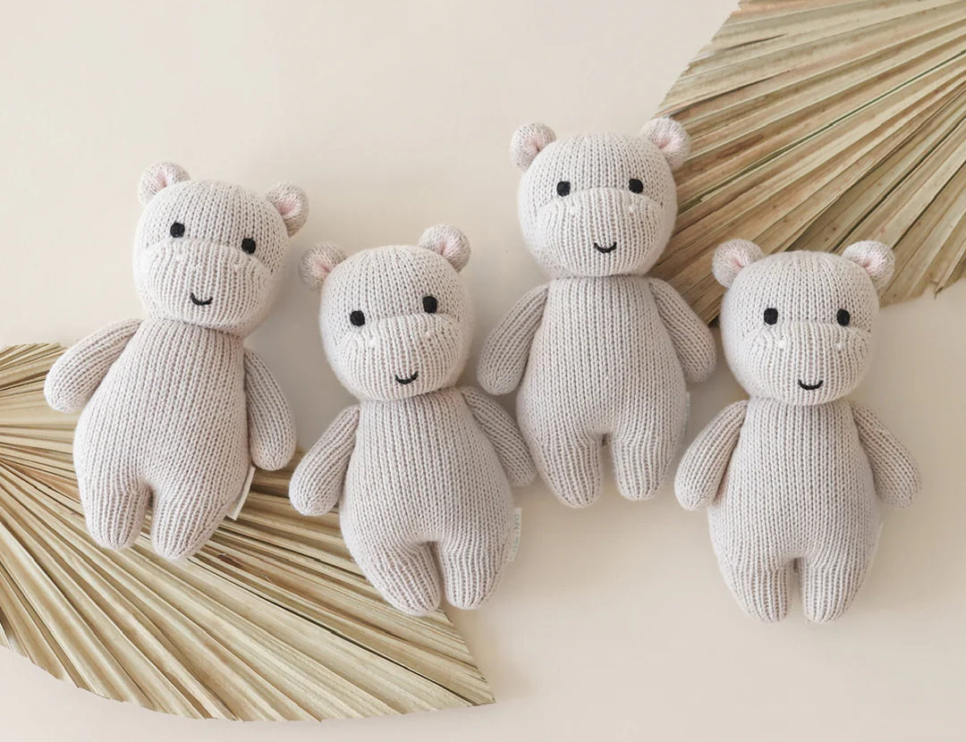 Cuddle & Kind Baby Hippo knit dolls, four cream hippos arranged with dried palm leaves