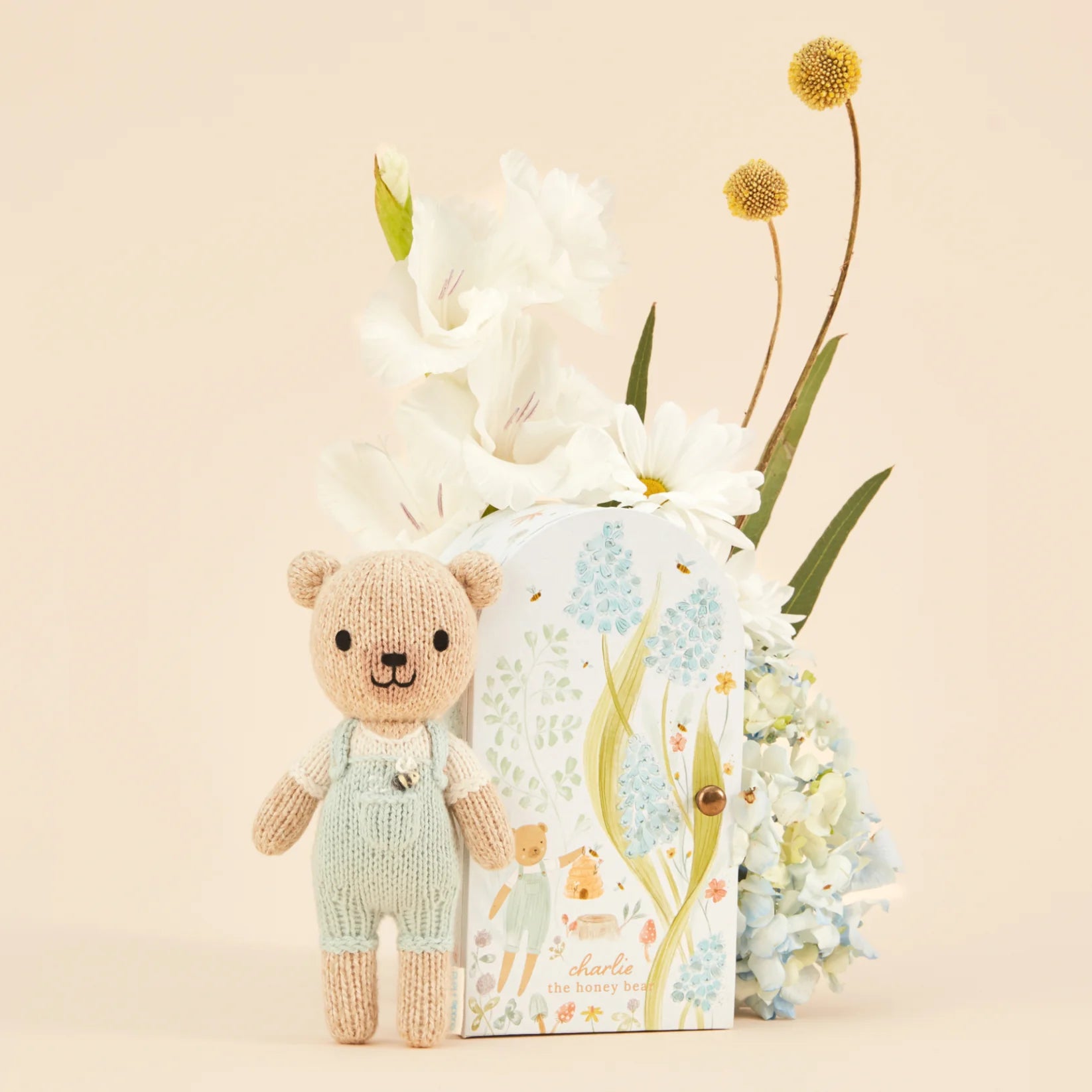 Cuddle + Kind Tiny Charlie the Honey Bear beside its gift box with white flowers