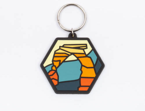 Delicate Arch keychain, a hexagonal soft rubber tag with the arch in orange and cream on teal and gold, on a silver split ring.