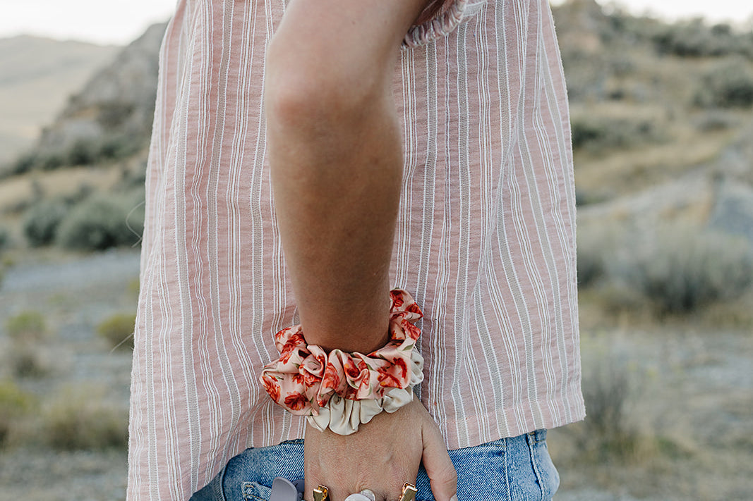 Desert Sol Satin Silk Scrunchie in Apricot Floral on a wrist, with hair clips in the back pocket
