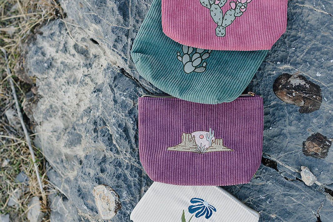 Desert Sol corduroy pouches in Prickly Mauve Pear, Mono Cactus, Desert Mesa and Night Bloom stacked on desert rock