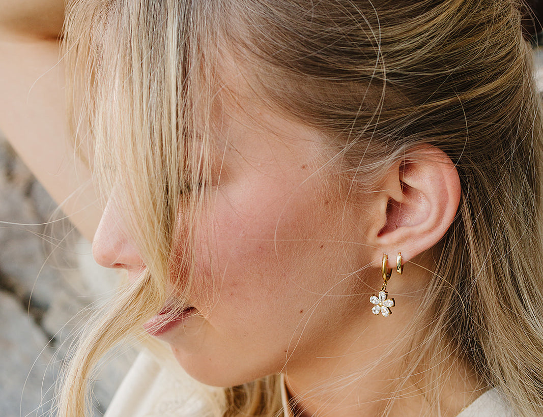 Close up of the Desert Sol Sundial Huggies in gold with a crystal flower drop earring, hand resting on her head