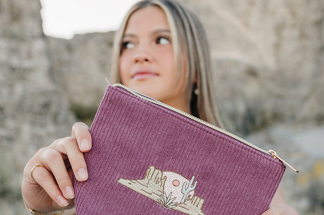 Model holding the Desert Sol Desert Mesa corduroy medium pouch in plum