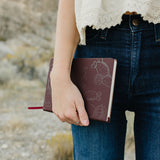 Desert Sol Meadow Ring on a hand holding the Desert Plum vegan leather journal against dark denim