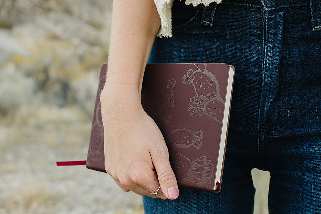 Desert Sol Meadow Ring on a hand holding the Desert Plum vegan leather journal against dark denim