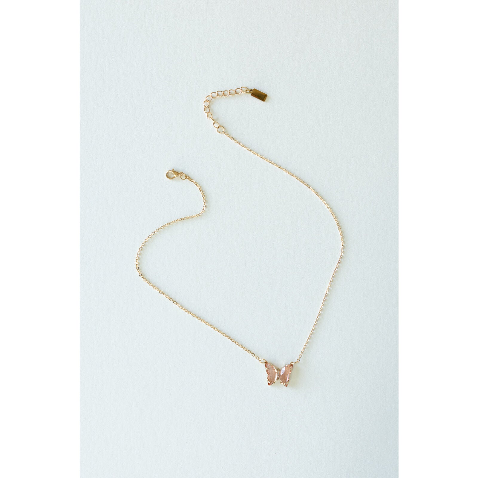 Desert Sol Ember Butterfly Necklace in blush pink, a faceted crystal butterfly pendant on a warm gold chain, on a white background