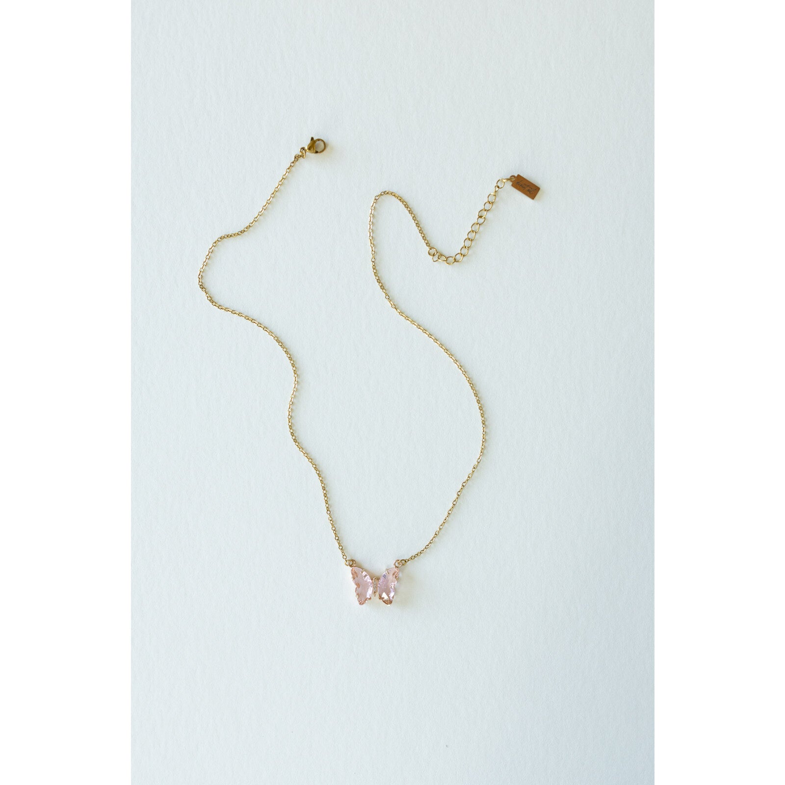 Desert Sol Ember Butterfly Necklace in blush pink, a faceted crystal butterfly pendant on a warm gold chain, on a white background
