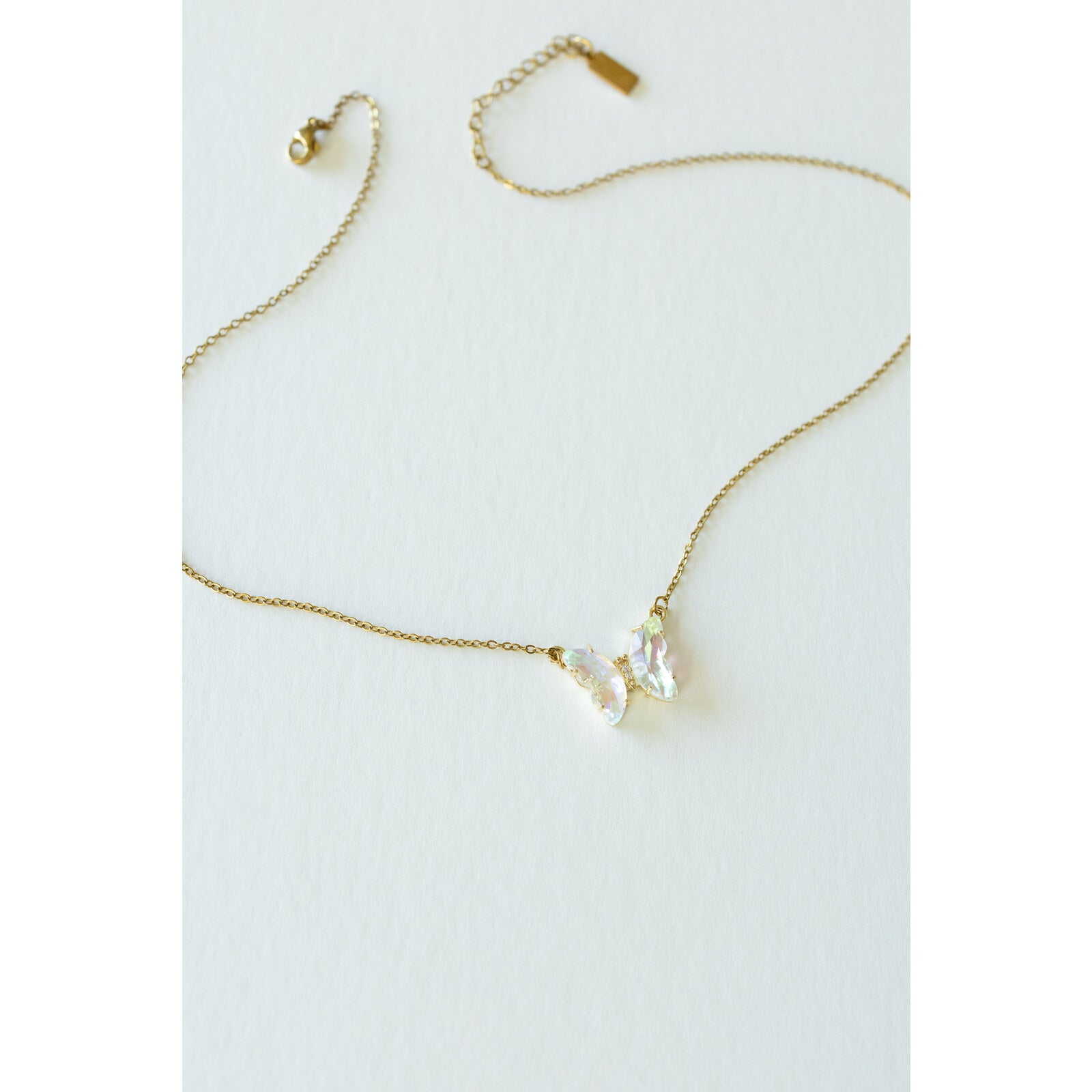 Desert Sol Ember Butterfly Necklace in opal white, a faceted crystal butterfly pendant on a warm gold chain, on a white background