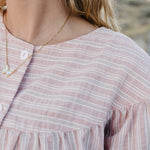 Close up of the Desert Sol Ember Butterfly Necklace in Opal White worn with a pink striped top