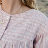 Close up of the Desert Sol Ember Butterfly Necklace in Opal White worn with a pink striped top