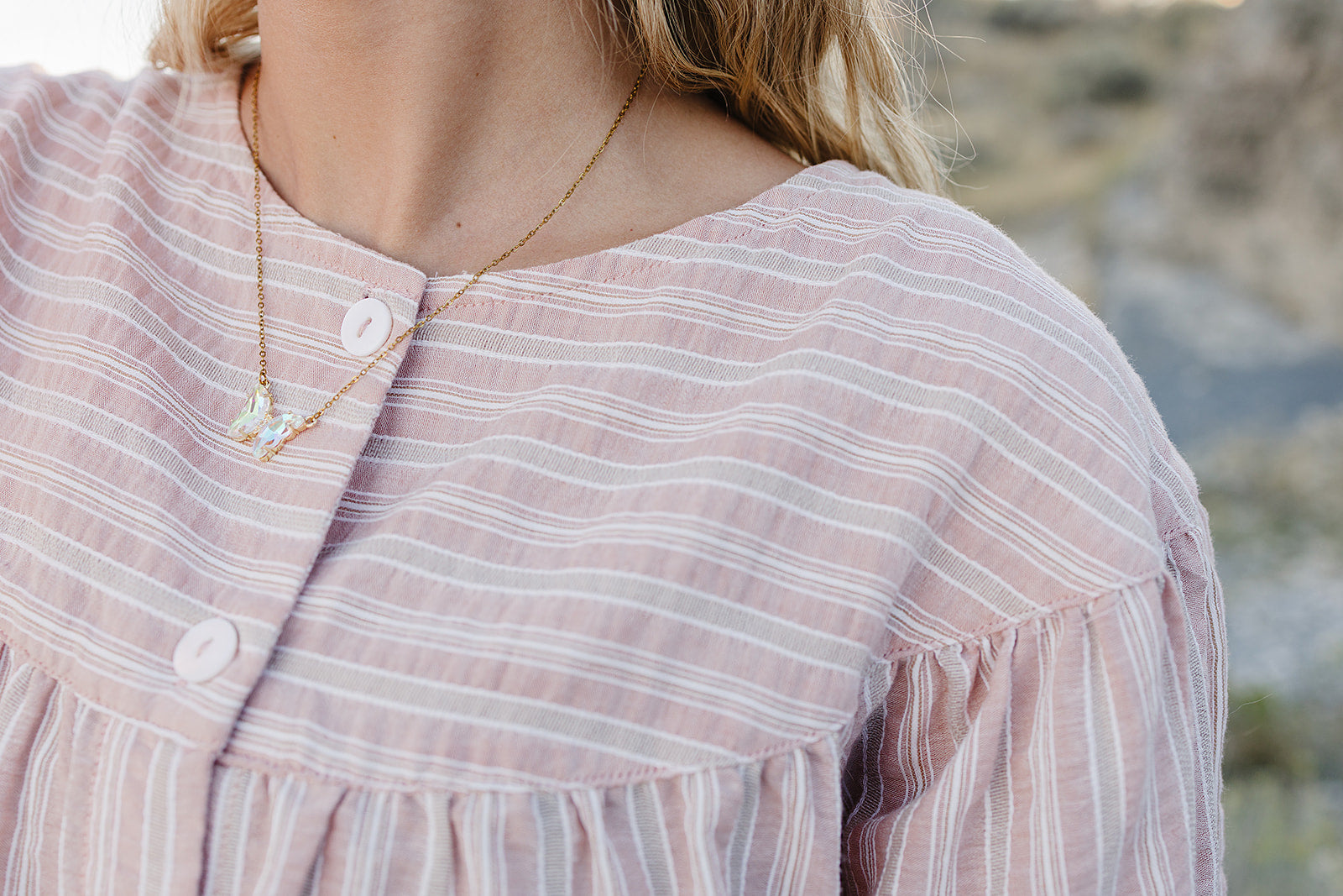 Close up of the Desert Sol Ember Butterfly Necklace in Opal White worn with a pink striped top