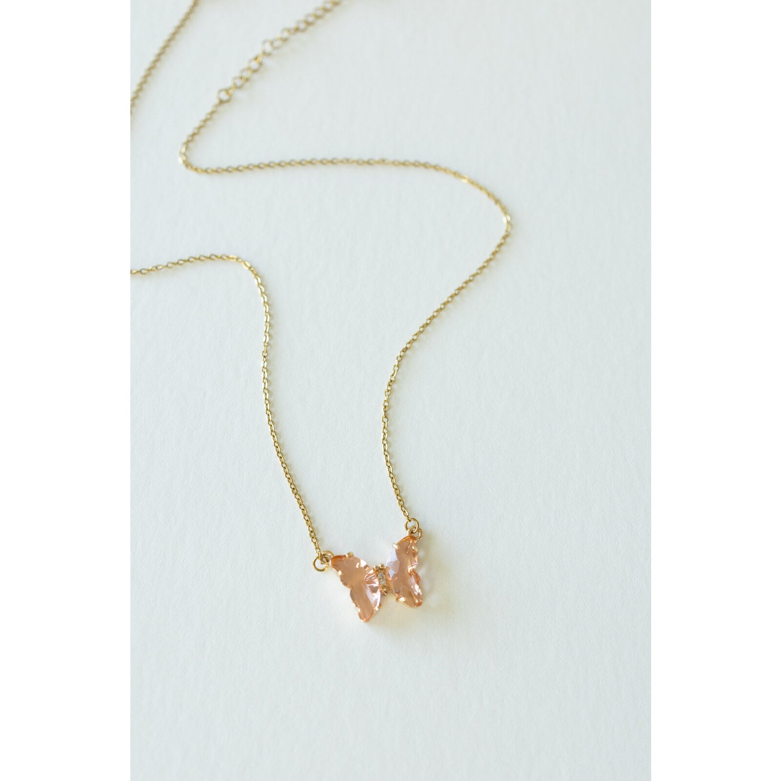 Desert Sol Ember Butterfly Necklace in peach, a faceted crystal butterfly pendant on a warm gold chain, on a white background