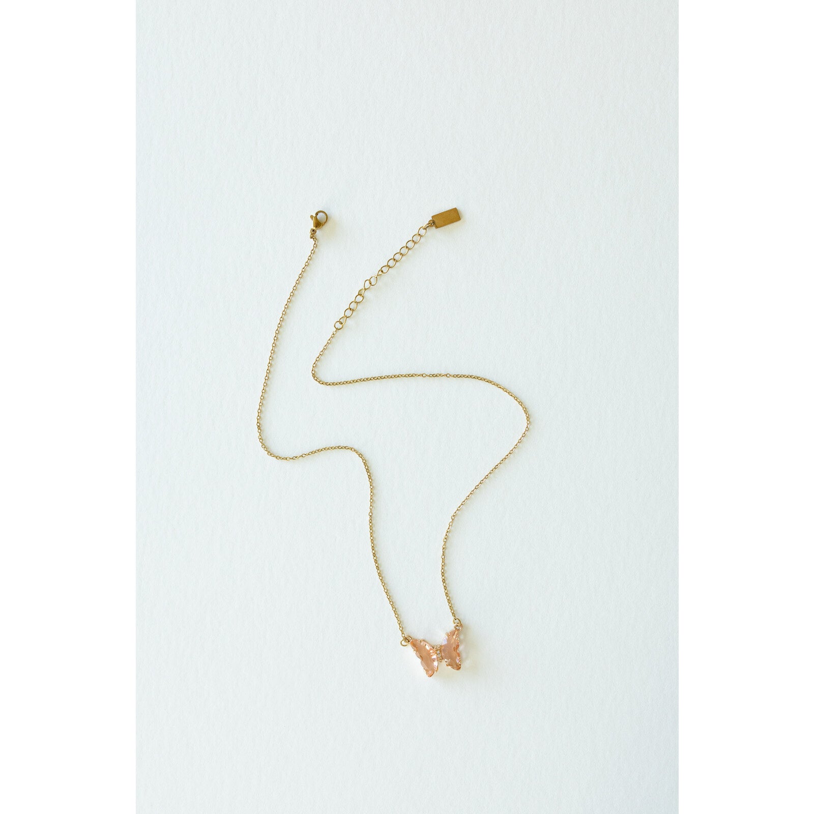 Desert Sol Ember Butterfly Necklace in peach, a faceted crystal butterfly pendant on a warm gold chain, on a white background