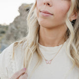 Model wearing the Desert Sol Everflight Butterfly Necklace in Petal Pink with a cream top