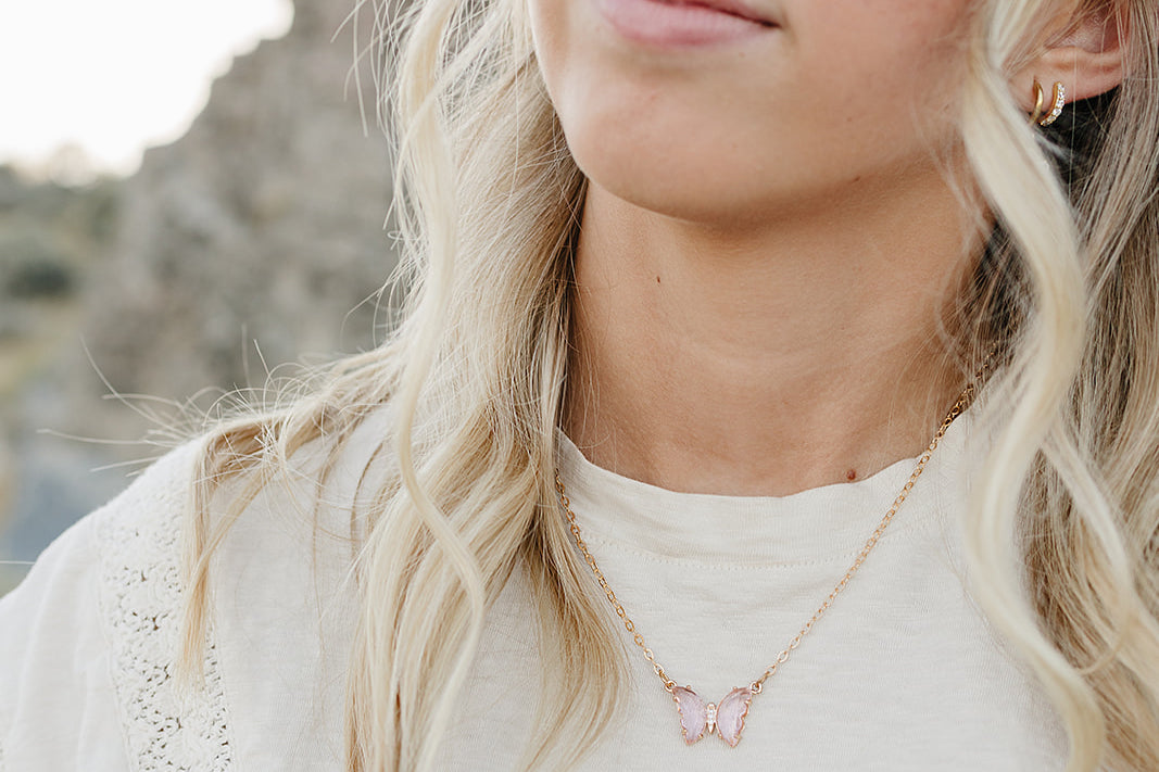 Model wearing the Desert Sol Everflight Butterfly Necklace in Petal Pink with a cream top