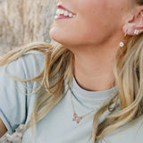 Smiling model wearing the Desert Sol Everflight Butterfly Necklace in Petal Pink with a sage tee
