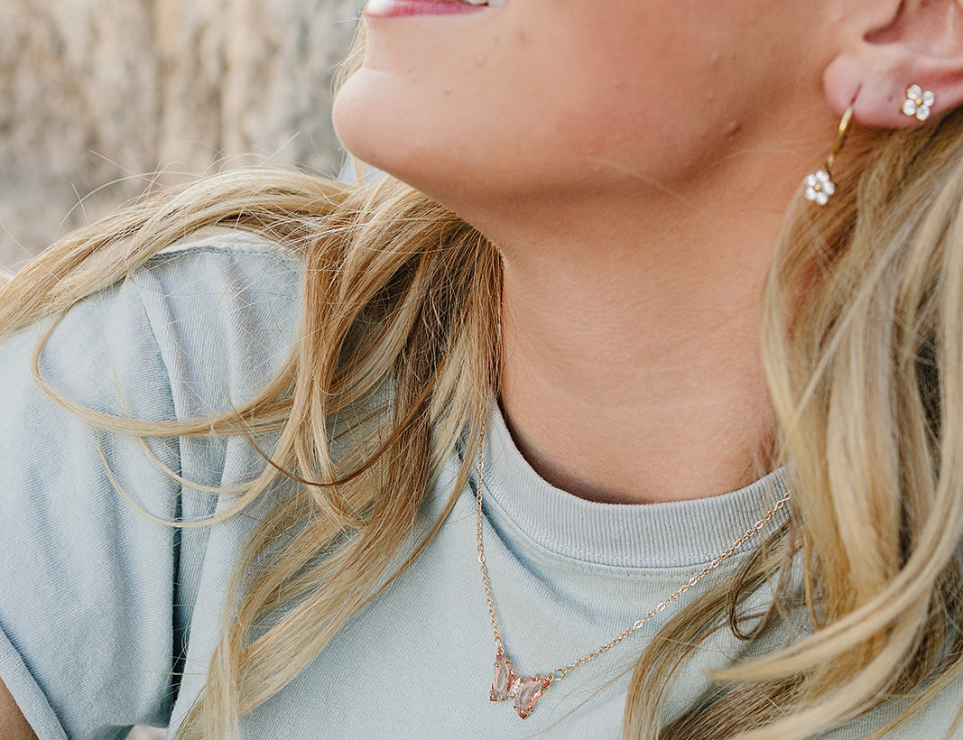 Smiling model wearing the Desert Sol Everflight Butterfly Necklace in Petal Pink with a sage tee