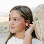 Model wearing the Desert Sol Fleur Hoop Earrings in gold, Sundust Pave Huggies and the Ember Butterfly Necklace in Blush Pink