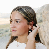 Model wearing the Desert Sol Fleur Hoop Earrings in gold, Sundust Pave Huggies and the Ember Butterfly Necklace in Blush Pink