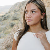 Model against desert rock wearing the Desert Sol Fleur Hoop Earrings in gold and a pink butterfly necklace
