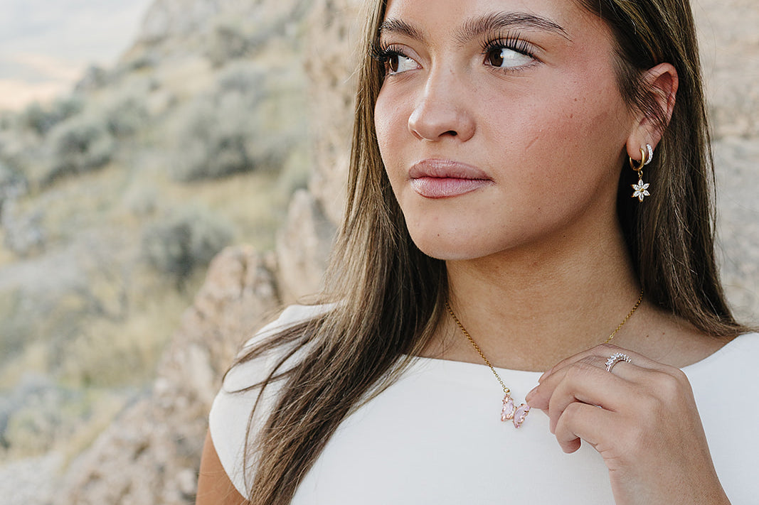 Model against desert rock wearing the Desert Sol Fleur Hoop Earrings in gold and a pink butterfly necklace