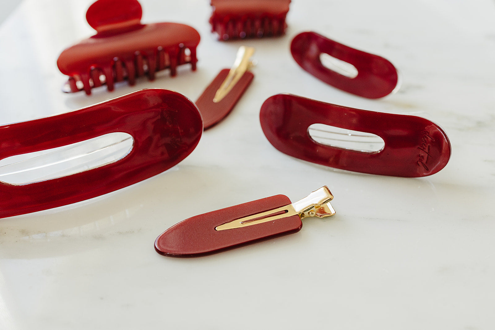 Desert Sol Garnet acrylic hair clip set with an oval lay flat claw clip, classic claw clip, petal claw clip and snap clips in deep red on white marble