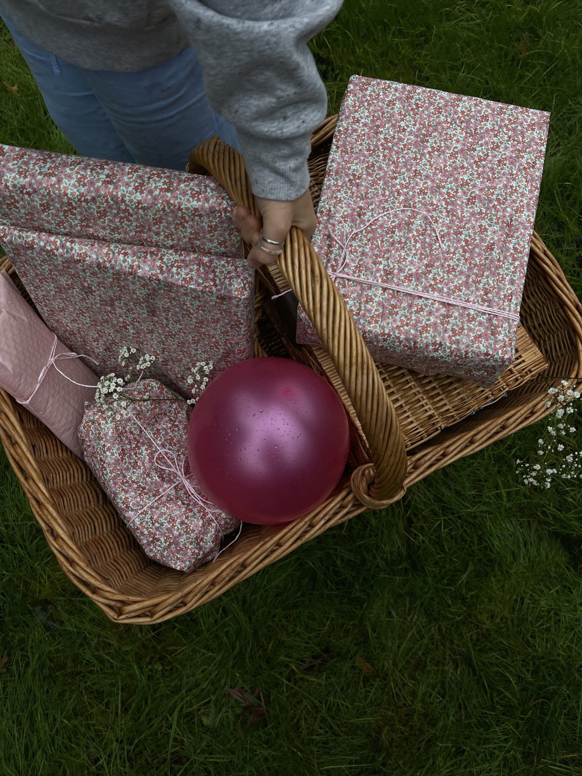 Gifts wrapped in pink floral paper and tied with pink string in a wicker basket with baby's breath and a pink balloon