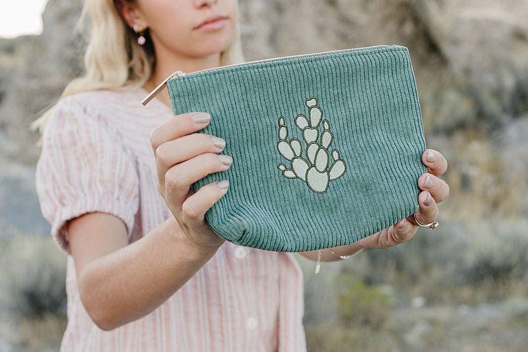 Model holding the Desert Sol Mono Cactus corduroy medium pouch in green