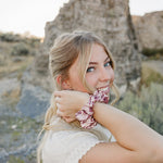 Model smiling with the Desert Sol Satin Silk Scrunchie in Mulberry Floral on her wrist