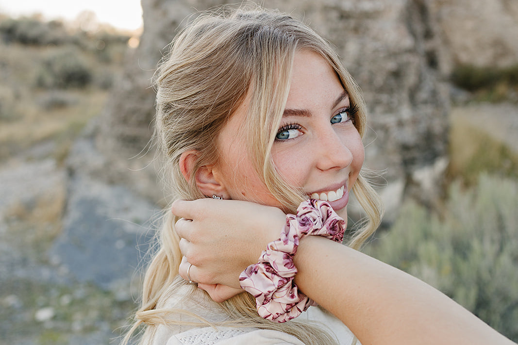 Model smiling with the Desert Sol Satin Silk Scrunchie in Mulberry Floral on her wrist