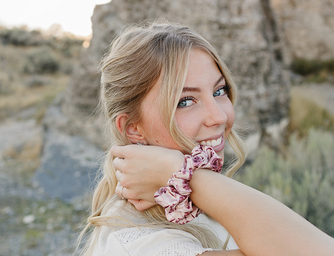 Model smiling with the Desert Sol Satin Silk Scrunchie in Mulberry Floral on her wrist