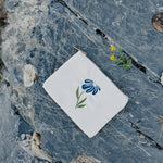 Desert Sol Night Bloom corduroy flat pouch with a blue embroidered flower lying on gray desert rock