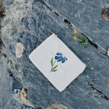 Desert Sol Night Bloom corduroy flat pouch with a blue embroidered flower lying on gray desert rock