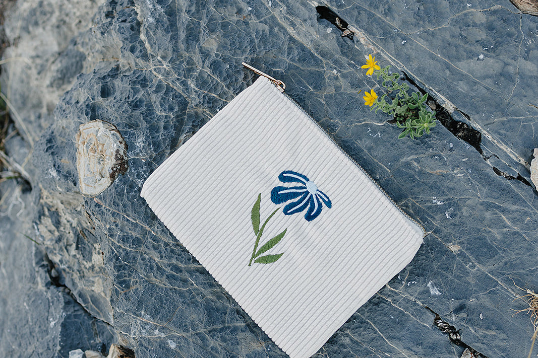 Desert Sol Night Bloom corduroy flat pouch with a blue embroidered flower lying on gray desert rock