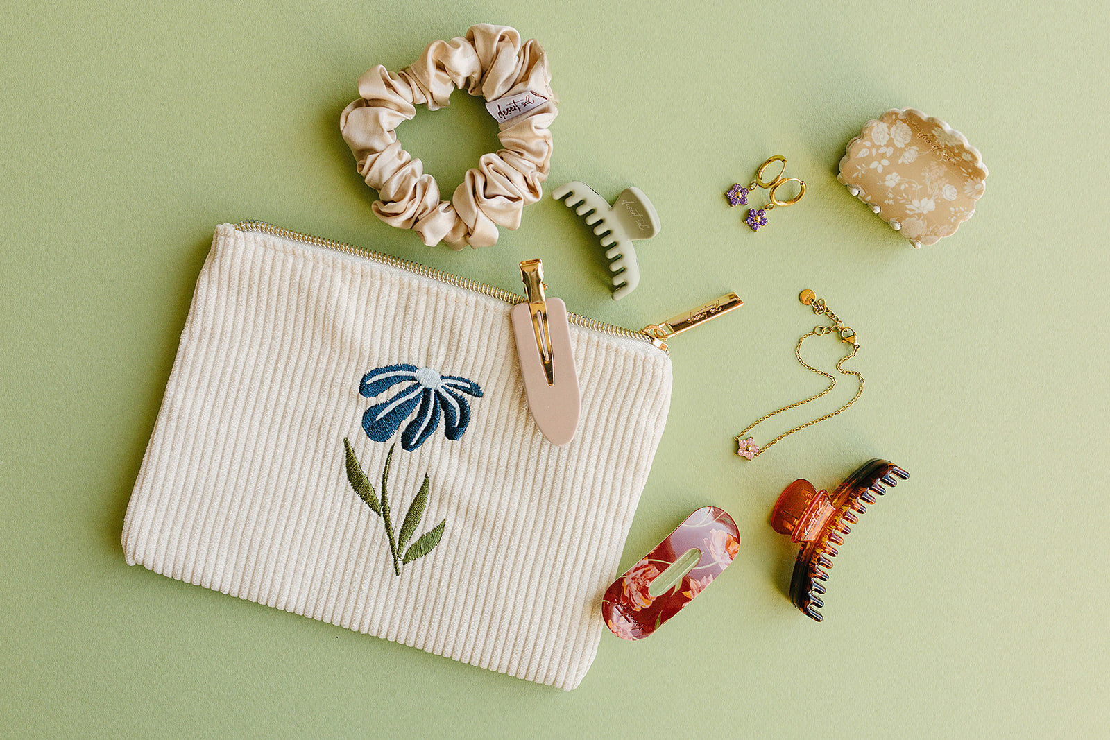 Desert Sol Night Bloom corduroy flat pouch styled with a scrunchie, claw clips and gold jewelry on a sage green background