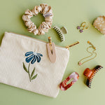 Desert Sol Night Bloom corduroy flat pouch styled with a scrunchie, claw clips and gold jewelry on a sage green background