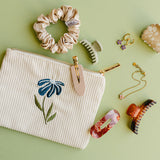 Desert Sol Night Bloom corduroy flat pouch styled with a scrunchie, claw clips and gold jewelry on a sage green background