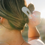 Close up of the Desert Sol Oval Lay Flat Acrylic Claw Clip in Pearl in a low bun at sunset
