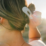 Close up of the Desert Sol Oval Lay Flat Acrylic Claw Clip in Pearl in a low bun at sunset