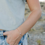 Desert Sol Petal Bracelet in gold with a pink crystal flower on a wrist by a jeans pocket