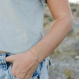 Desert Sol Petal Bracelet in gold with a pink crystal flower on a wrist by a jeans pocket