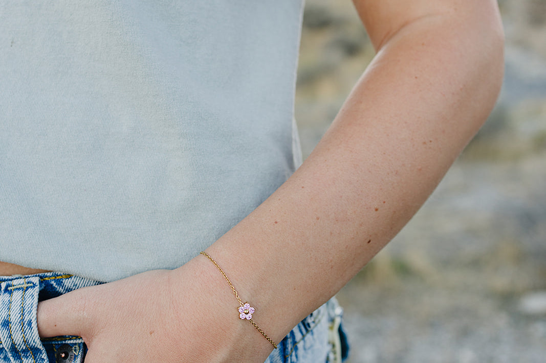 Desert Sol Petal Bracelet in gold with a pink crystal flower on a wrist by a jeans pocket